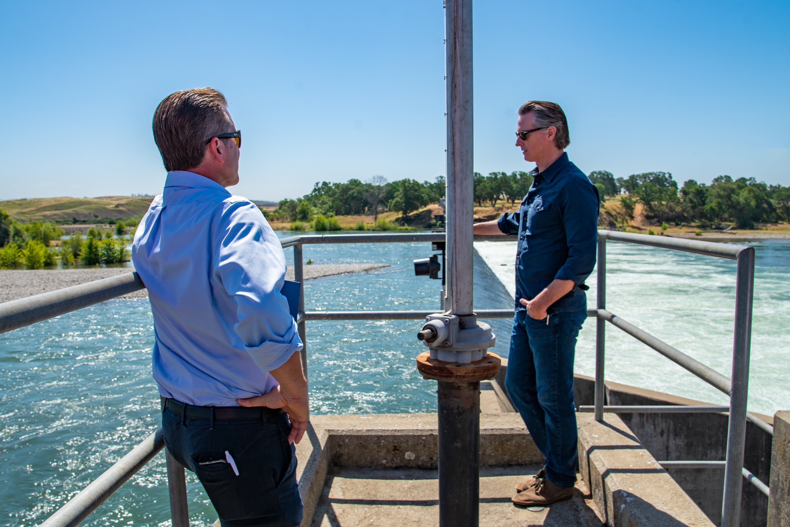 Two men stand on a concrete pad looking down at the Lower Yuba River and Daguerre Point Dam.