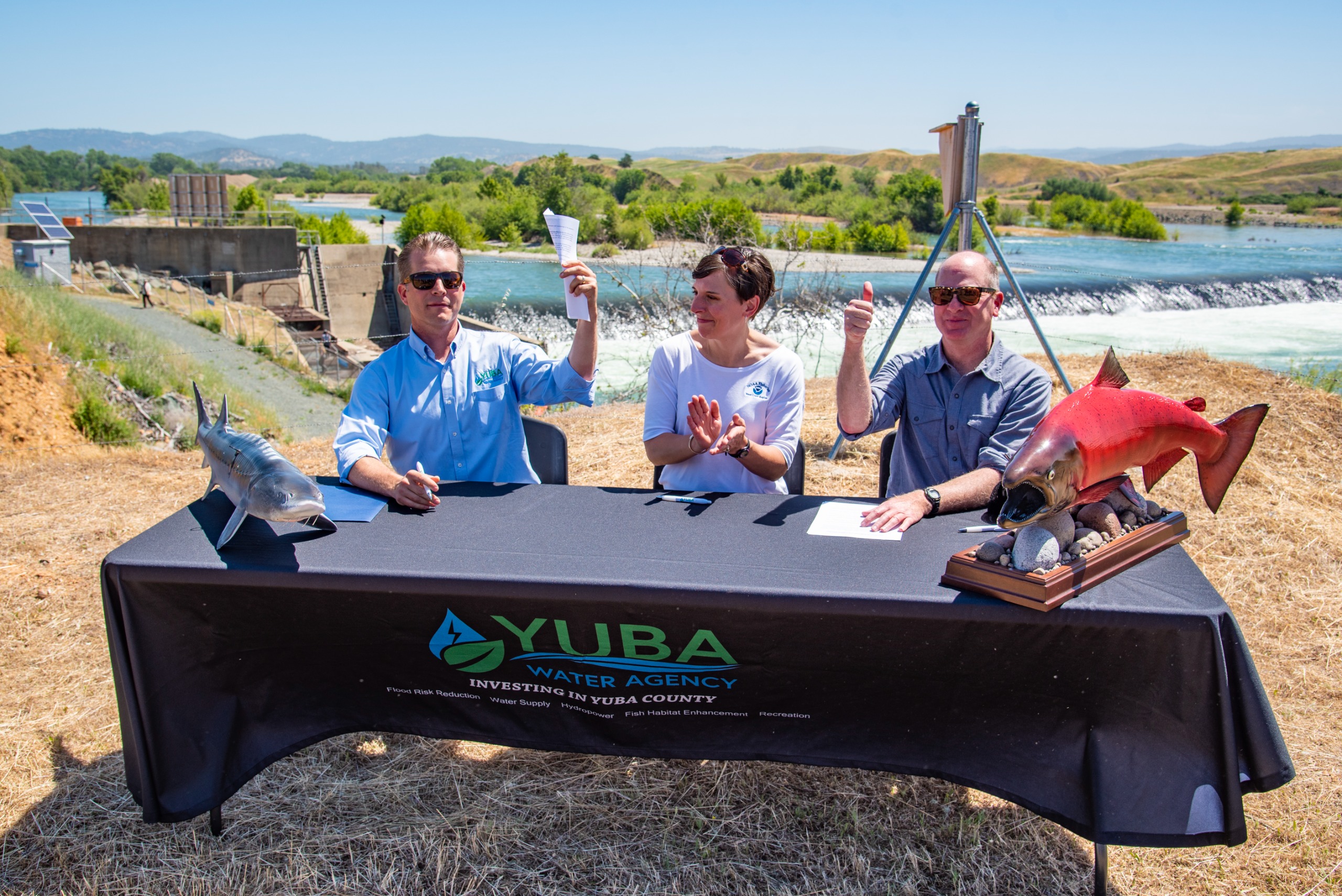 Two men and a woman sit at a table holding up freshly signed papers. 